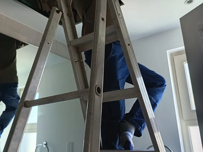 Technician on a ladder accessing a ducted AC unit through a ceiling hatch