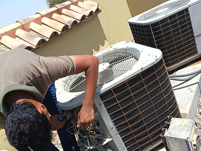 Haji AC technician repairing the fan wiring of a rooftop package unit at a UAE villa