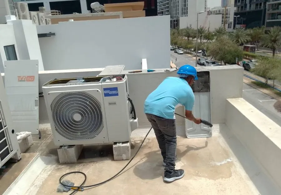Haji AC technician pressure-cleaning a rooftop condenser unit at a Dubai property
